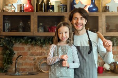 Pişirme Günü. Mutlu genç baba ve küçük kızı ellerinde oklavayla mutfakta poz veriyorlar.