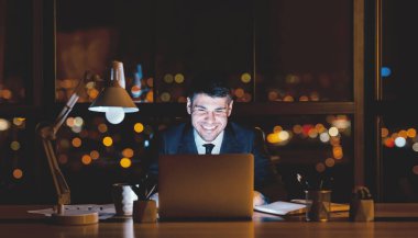 Business Lifestyle. Smiling Businessman Working On Laptop At Workplace At Night. Panorama clipart