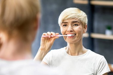 Diş temizleme. Dişlerini fırçalarken diş fırçası kullanan kadın banyoda dikiliyor. Seçici Odaklanma, Boşluk Boşluğu