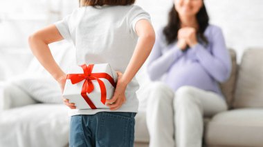 Hamile annesi için hediye kutusuyla küçük bir kız, Anneler Günü 'nde annesini selamlayan bir kız.