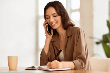 Kadın Asistanı. Modern ofiste cep telefonuyla konuşan ve notlar yazan genç ve güzel bir resepsiyonist.