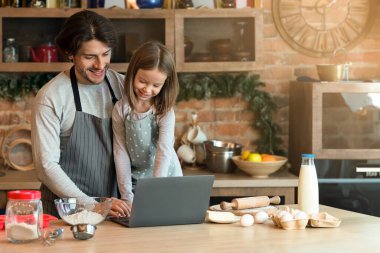 Küçük tatlı bir kız, babasıyla birlikte dizüstü bilgisayar kullanıyor, kurabiye tariflerini kontrol ediyor, fırını birlikte hazırlıyor, ev yapımı hamur işleri yapıyor, uzay kopyaları yapıyor.