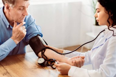 Kardiyoloji. Meksikalı doktor yaşlı adamın kan basıncını ölçüyor, hastayı kontrol ediyor, boş yer var.