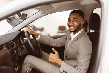 Harika araba. Afrikalı İşadamı Oto galerisindeki Sürücü Koltuğu 'nda Otururken Başparmağıyla İşaret Ediyor. Seçici Odaklanma