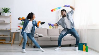 Temizlik eğlencesi. Neşeli siyah çift dairelerini toplarken, tozluk ve süpürgelerle oyun oynarken, evde otururken, boş alan ararken eğleniyorlar.