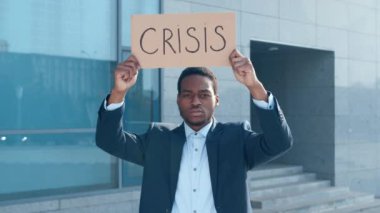 Takım elbiseli Afro-Amerikan bir adam, çağdaş bir mimari yapı önünde kriz yazan bir tabela kaldırıyor..