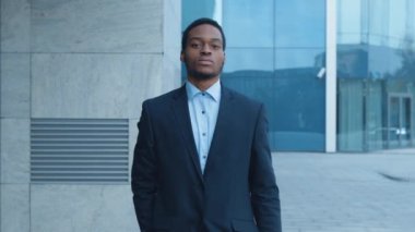 İyi giyimli, takım elbiseli bir Afro-Amerikan adam şehrin kaldırımında çağdaş bir cam binanın yanında kasten yürüyor..