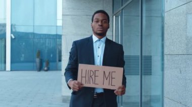 Afro-Amerikalı bir adam bir ofis binasının önünde duruyor, elinde 