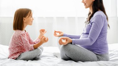 Sağlıklı aile kavramı. Anne ve kızının birlikte sabah yogası yapmasını, yüz yüze yatakta oturmasını beklemek.