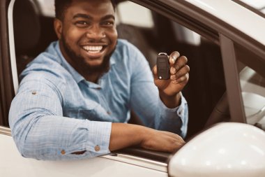 Black Guy Showing Car Key Smiling To Camera Sitting In New Automobile. Happy Auto Buyer. Selective Focus