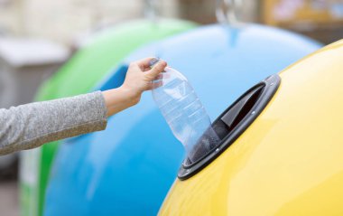 Atık Geri Dönüşüm Konsepti. Tanınmayan bir kadın, sarı geri dönüşüm kutusuna plastik şişe atıyor, çöpleri ayırıyor, sıfır atıkla yaşıyor, seçici odaklı kırpılmış görüntüden keyif alıyor.