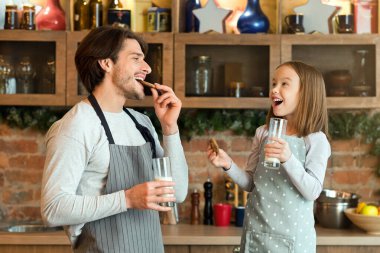 Atıştırma zamanı. Neşeli baba ve küçük kız taze pişmiş kurabiye yer ve mutfakta süt içerler, ev yapımı hamur işlerinin tadını çıkarırlar, önlük giyerler ve birbirlerine gülümserler, evde eğlenirler, uzay kopyalarlar.