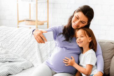 Mutlu bir kadının küçük kızıyla selfie çekmesini beklerken evdeki kanepede boş boş boş otururken.