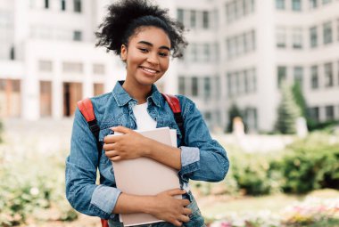 Başarılı Öğrencinin Portresi. Dışarıda modern üniversite binasının yanında duran kameraya gülümseyen mutlu Afrikalı Amerikalı genç kız poz veriyor. Öğrencilik, Modern Eğitim