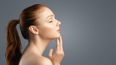 Kadın Güzellik Portresi. Tişörtsüz, kızıl saçlı, at kuyruklu, saçları at kuyruklu, gözleri kapalı çeneye dokunan genç bayanın yan görüntüsü. Stüdyo Çekimi