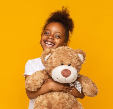 En sevdiğim oyuncak. Sevimli küçük afrikalı kız onu oyuncak ayı sarılma ve gülümseyen, turuncu stüdyo arka plan