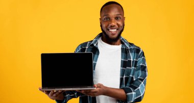 Gülümseyen Afrikalı Adam Laptop Boş Ekranı Sarı Stüdyo Arkaplanında Duran Harika Web Sitesini Öneren Kameraya Gösteriyor. Çevrimiçi Servis Reklamı. Model