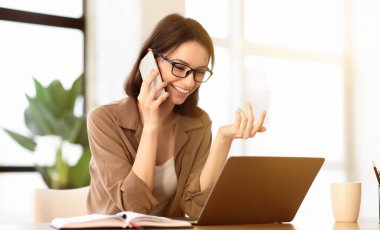 İş görüşmesi. Cep telefonuyla konuşan mutlu bir kadın, danışmanlık yapan bir müşteri, dizüstü bilgisayar, el kol hareketi, kopyalanma...