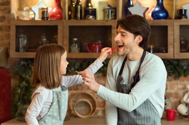Genç babasını ve küçük kızını sevmek mutfakta sebze salatası pişirirken birbirlerini beslemek, sağlıklı yiyecekler tatmak.