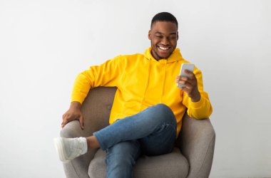 Neşeli Siyah Milenyum Adamı Cep Telefonu Tarama İnterneti ve Kapalı Kapılar Arasındaki Kol Sandalyesinde Oturan Mesaj Kullanıyor. İnsanlar ve Gadget 'lar. Mobil İletişim Konsepti