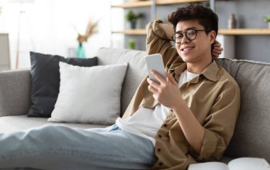 Hafta sonunun tadını çıkarıyorum. Gözlüklü yakışıklı Asyalı adam evde otururken akıllı telefon kullanıyor, mutlu adam oturma odasında dinleniyor, internete bakıyor ya da arkadaşlarıyla mesajlaşıyor, seçici odaklanıyor.