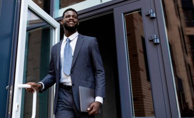 Genç Afrikalı Amerikalı girişimci işten sonra iş merkezini terk ediyor, başka tarafa bakıyor ve gülümsüyor, mekanı kopyalıyor. İş adamları ve başarılı kariyer kavramı