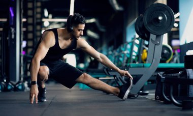 Spor salonunda antrenman öncesi ısınan yakışıklı genç Orta Doğulu erkek sporcu, Milenyum Arap erkeğinin bacak kaslarını esnetmesi, modern spor kulübünde spor yapmaya hazırlanması,