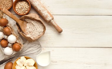 Maddeler arka plan yemek. Un, yumurta, Kuru üzüm, şeker, süt, tereyağı ve mutfak eşyaları kopya alanı ile beyaz rustik ahşap üzerine sınır. Hamur hazırlama ve pasta kavramı, üstten görünüm