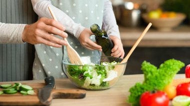 Baba ve küçük kız birlikte sebze salatası pişiriyorlar, zeytinyağı ekliyorlar, kırpılmış görüntü, yakın plan.