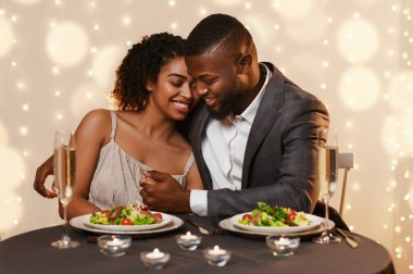 Yakışıklı siyahi adam, güzel kadınını kucaklarken bir yandan da restoranda akşam yemeği yiyor. Sevgililer Günü konsepti.