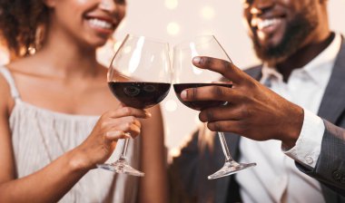 Kırmızı şarapla kadeh kaldıran, yıldönümünü kutlayan neşeli Afro-Amerikan çiftlerine yakın durun.