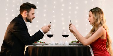 Modern Tarih Konsepti. Erkek ve kadın telefonlarıyla vakit geçiriyorlar, romantik bir randevuda restoranda birbirlerini görmezden geliyorlar, yan gözle bakıyorlar.
