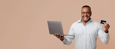 Kredi kartı tutan, bilgisayarla ödeme yapan, turuncu stüdyo geçmişi olan mutlu bir afro adam.