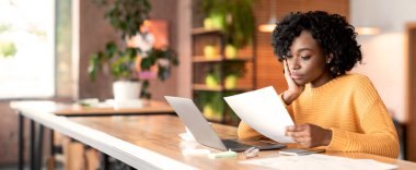 Concentrated afro girl professional editor working with text at cafe, using laptop, empty space