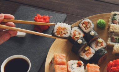 Japon yemek restoranı, suşi maki rulo plaka, tabak seti. El rulo almak. Yemek çubukları, zencefil, soya, wasabi ile iki ayarlayın. Rustik ahşap arka plan ve siyah taş suşi. Pov siyahta. Closeup.