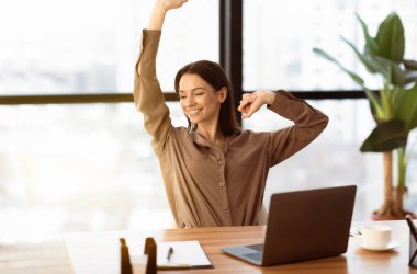 Stiff Neck 'ten kurtul. Kahverengi uzun kollu gömlekli gülümseyen genç bir kadın ofisteki masanın önünde geriniyor.