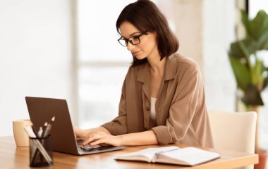 Dalgın İşçi. Gözlüklü gülümseyen kızın portresi dizüstü bilgisayar kullanıyor, ofiste oturuyor ve araştırma yapıyor.