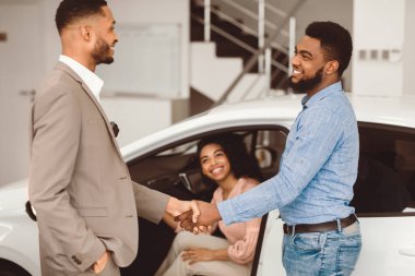 Siyah adam otomobil galerisinde araba satıcısıyla tokalaşıyor karısıyla araba satın alıyor. Seçici Odaklanma