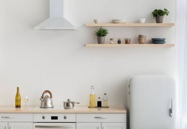 İskandinav tarzında, basit, minimalist iç mimari tarzında modern minimalist beyaz mutfak. Buzdolabı, çanak çömlekli raflar, saksılarda bitkiler, mobilyalar ve çatal bıçaklı soba, ışık duvarı, boş alan.