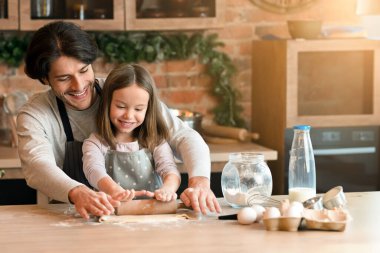 Küçük Yardımcı. Mutlu baba ve anaokulu kızı birlikte hamuru sarıyorlar, mutfakta eğleniyorlar, pasta pişiriyorlar, bedava yer açıyorlar.