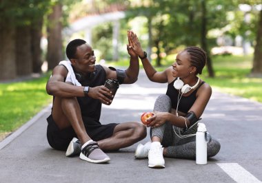 İlişki Hedefleri. Başarılı açık hava eğitiminden sonra aktif Afrikalı çift, parkta dinlenirken birbirlerine beşlik çakıyor.