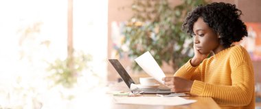 Kadın girişimci siyahi bayan, kafede belgelerle çalışıyor, laptop kullanıyor.