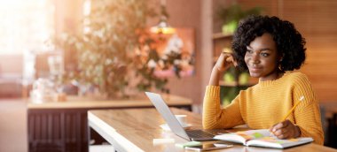 Yaratıcı serbest çalışan Afrikalı kız yeni bir proje düşünüyor, notlar alıyor, laptopla kafede çalışıyor, uzayı kopyalıyor.