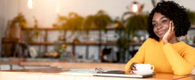 Kafede yalnız başına kahve molası veren dalgın siyah bir kadın, boş bir alana yaslanmış.