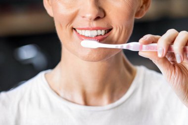 Sabahın köründe diş fırçası ve diş macunu kullanan neşeli, olgun bir kadın tuvalette dikiliyor. Diş sigortası ve hijyen. Panorama