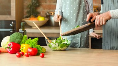 Aile yemekleri. Neşeli baba ve küçük kız birlikte sağlıklı bir öğle yemeği hazırlıyorlar, salataya sebze ekliyorlar, babaya bakıyorlar, tatlı kıza yemek yapmayı öğretiyorlar, evde birlikte eğleniyorlar, uzayı kopyalıyorlar.