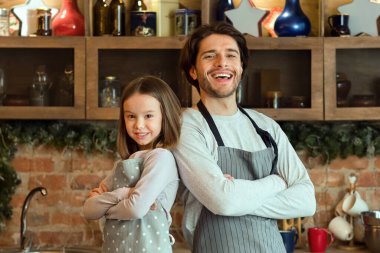 Pişirmeye hazırım. Kendine güvenen genç babası ve küçük kızı mutfakta önlük takıyor, sırt sırta verip kollarını kavuşturuyor ve uzayı kopyalıyor.