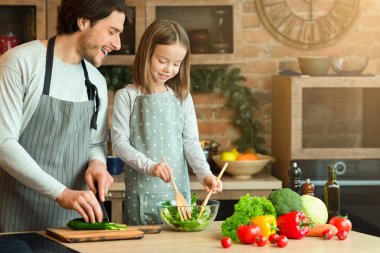 Aile Aşçılığı Konsepti. Yakışıklı genç baba küçük kızına sebze salatası pişirmeyi öğretiyor, mutfakta sağlıklı yiyeceklerin tadını çıkarıyor, bedava yer açıyor.