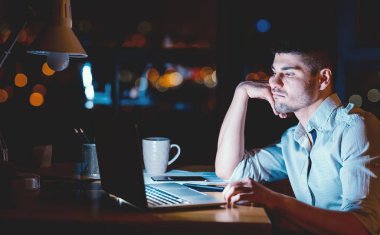 Gecelik iş. Laptop 'ta oturup Chin' e dokunan yorgun işadamı gece geç saatlere kadar modern ofiste çalışıyor. Düşük Işık