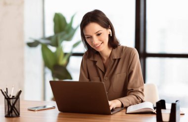 Studying With Music. Smiling female student wearing earphones and using personal computer, empty space